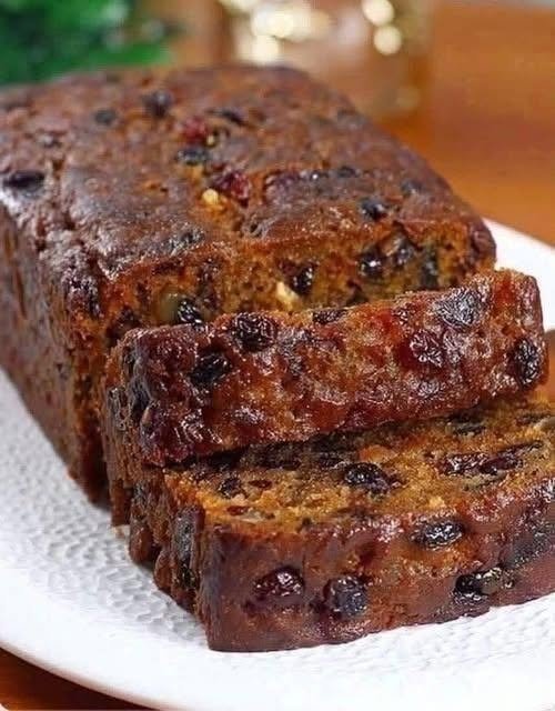 Moist homemade Apple Fruit Cake loaf with three apples, raisins, and warm cinnamon, sliced on a white serving plate.