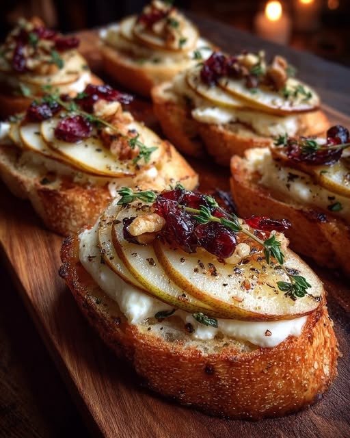 Pear Brie Crostini with creamy Brie, sliced pears, cranberries, walnuts, fresh thyme, and honey on toasted baguette